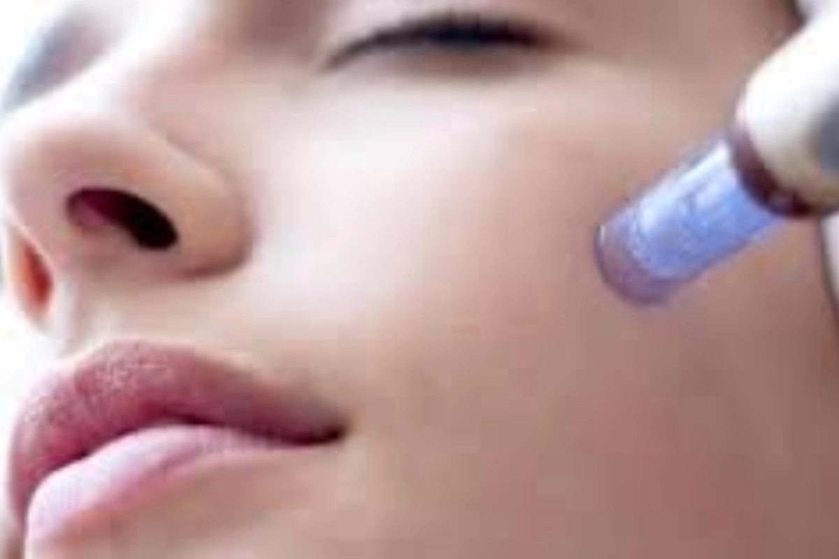 Close-up of a person's face undergoing a skin treatment with a blue-tipped device applied to the cheek.