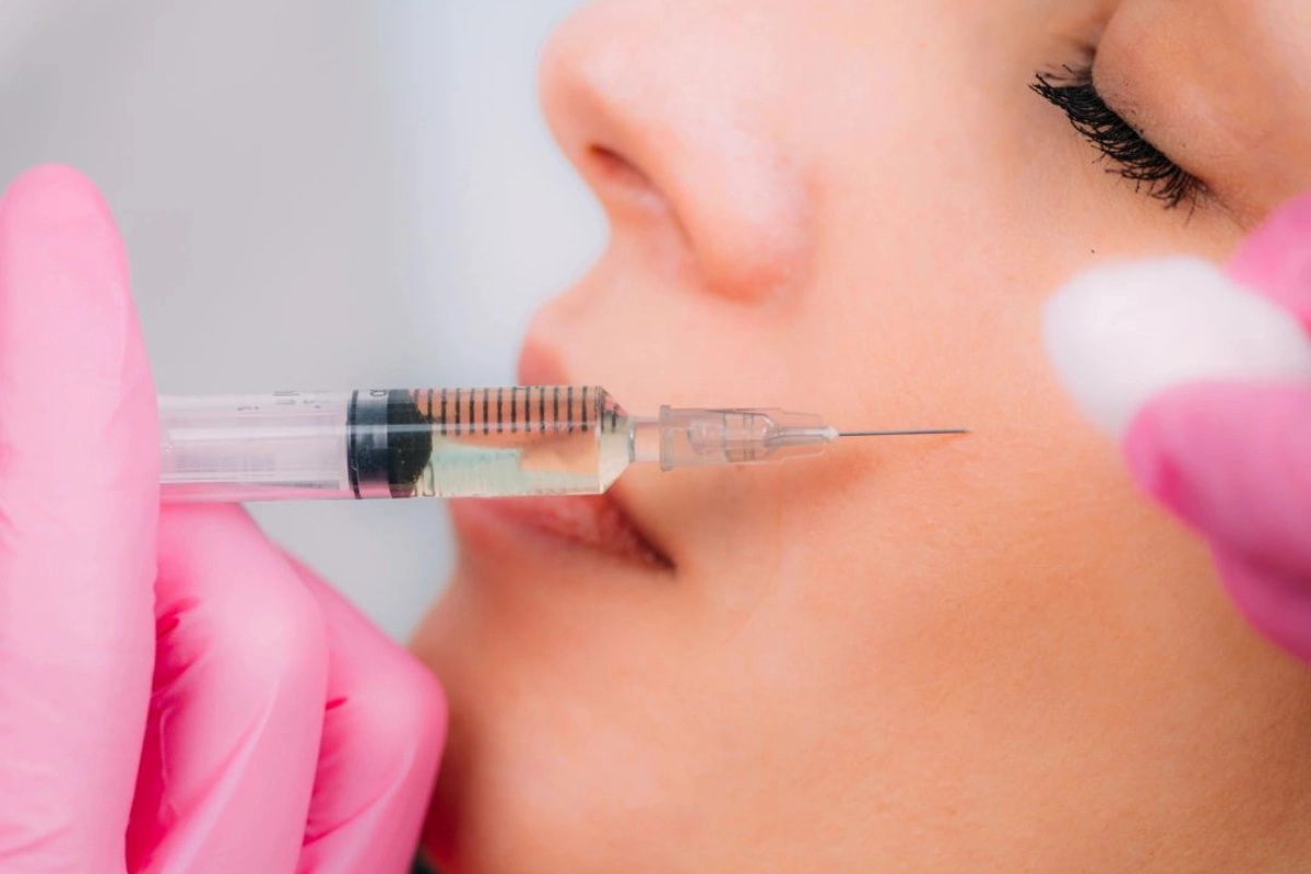 A person in pink gloves administers an injection to the cheek of a woman's face.