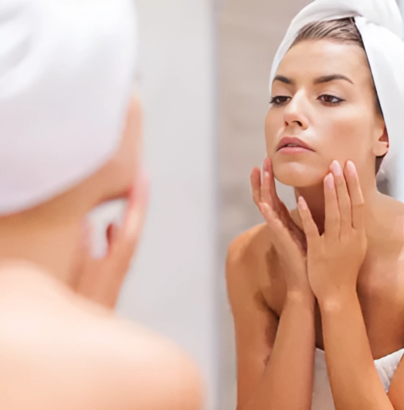 A woman with her hands on her face looking in the mirror.