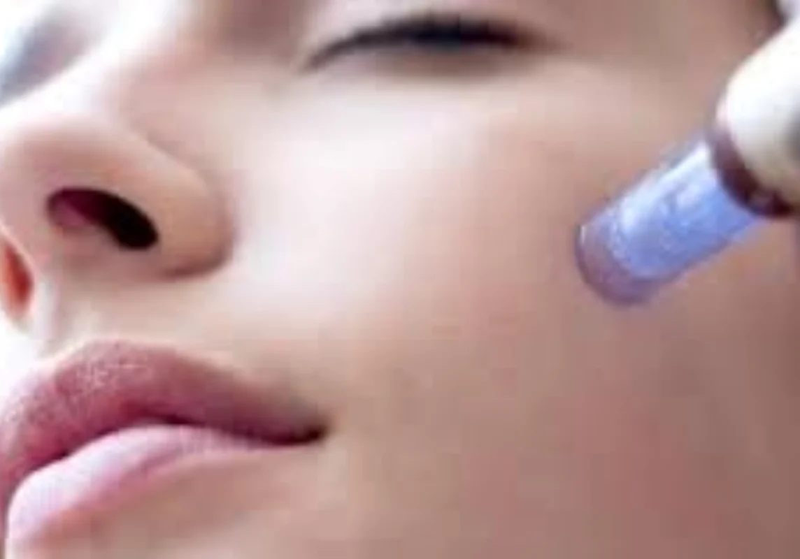 Close-up of a person's face undergoing a skin treatment with a blue-tipped device applied to the cheek.