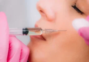 A person in pink gloves administers an injection to the cheek of a woman's face.